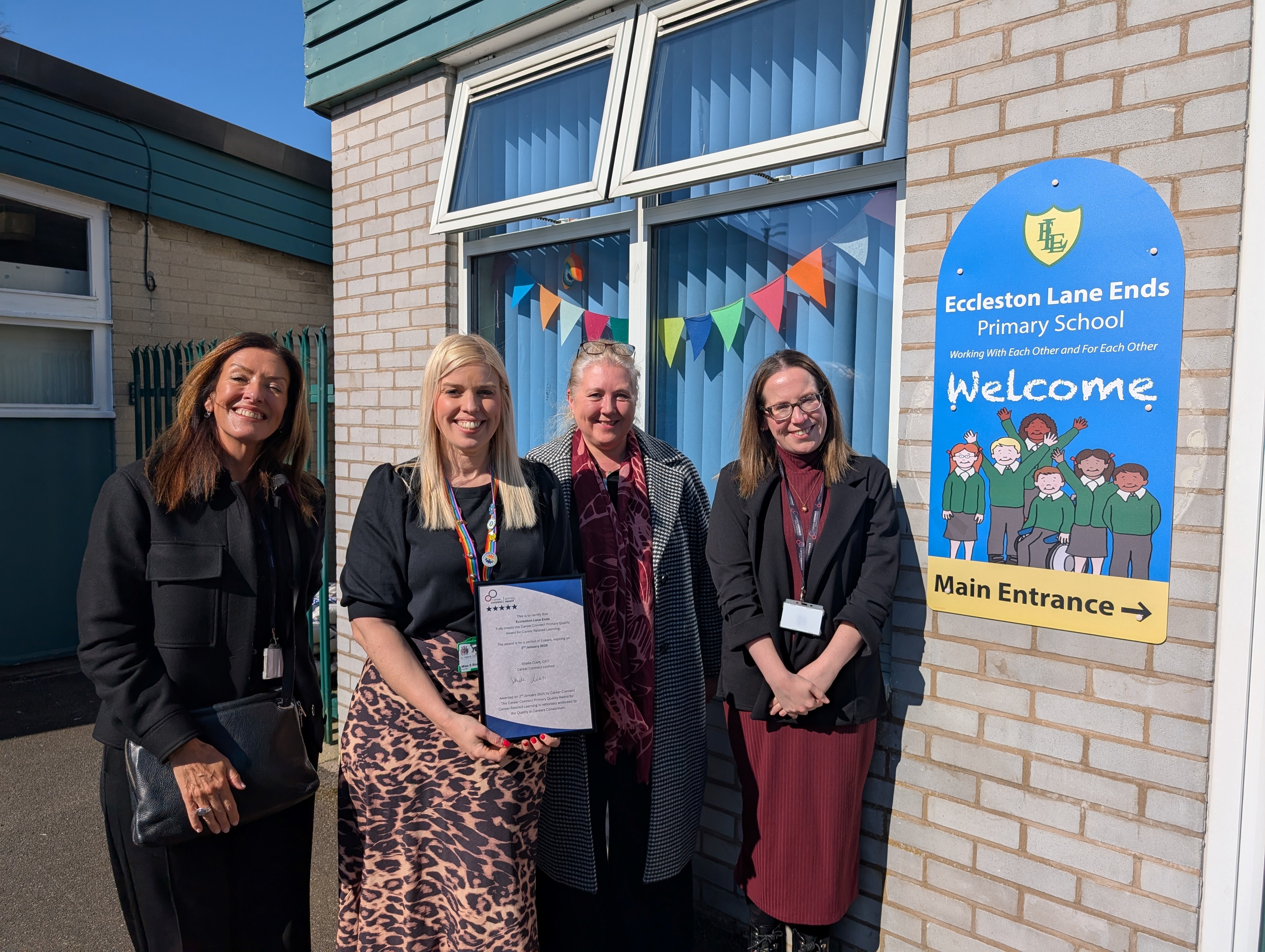 Two Career Connect staff, Eccleston Lane Ends Headteacher, and a visitor from DfE in front of Eccleston Lane Ends Primary School, with the Headteacher holding the Career Connect Primary Award Certificate.